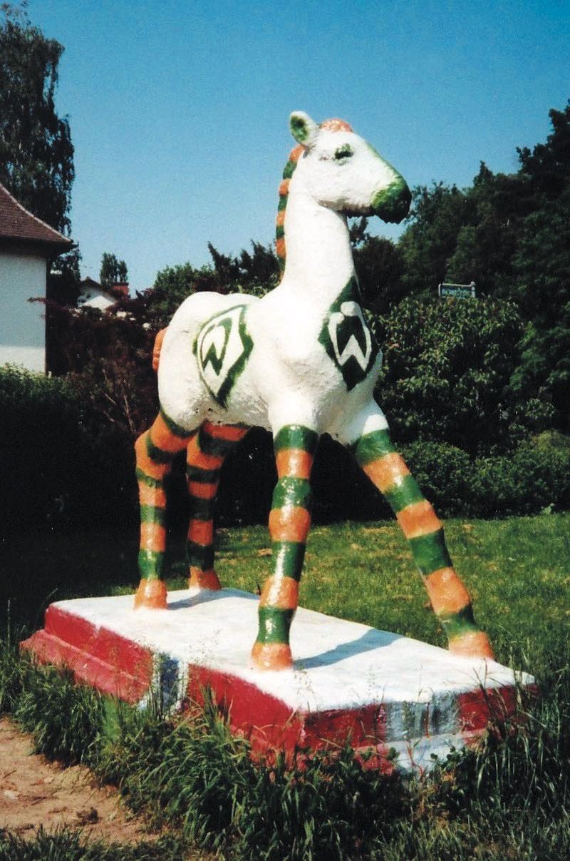 Holbein-Pferd weiß mit grün-orange geringelten Beinen und Werder-Logo auf rot-weißem Sockel